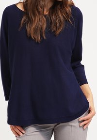 Námořnický modrý svetr vyrobený z měkké látky, s volným střihem, dlouhými rukávy, kulatým výstřihem a zaobleným lemem. Bez viditelných vzorů nebo akcentů.