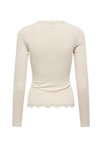 Pitkähihaisen kermaisen topin, jossa on ribbitekstuuria, koristeellinen pitsireuna kaula-aukossa ja helmassa, tiukka malli ja pehmeä materiaali.