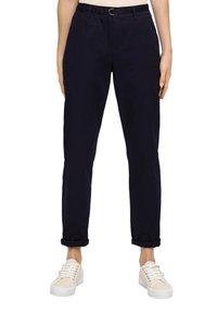 Pantalons en coton bleu marine à coupe droite, avec des poignets retroussés et une passant de ceinture avec un anneau en métal argenté. Associés à des baskets blanches à semelle basse.