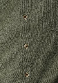 Groene gestructureerde stoffen shirt close-up, met plastic knopen met een cirkelvormig ontwerp en een borstzak.