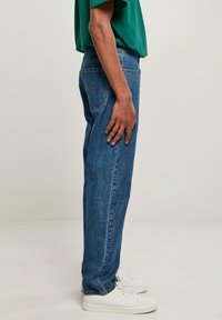 Vaqueros vaqueros azules de corte relajado, con cinco bolsillos y diseño de pierna recta. Combinados con zapatillas blancas y una camiseta verde.