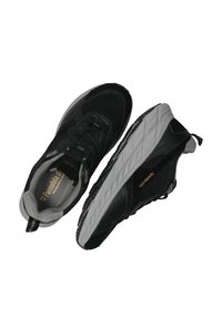 Baskets de sport noires avec une tige en maille et synthétique, semelle gris texturé, fermeture à lacets et détails de marque en or.