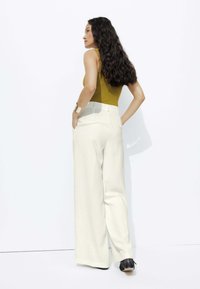 Pantalon blanc ample associé à un débardeur ajusté couleur moutarde. Texture douce et design soigné avec des poches visibles sur les côtés.