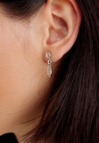 Boucles d'oreilles en argent avec un design en forme de goutte circulaire et texturée, ornées d'une pierre précieuse claire. Fixées avec un fermoir à ressort.
