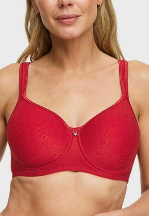 Vrouw draagt een rode, met patroon bedekte beha met verstelbare bandjes en een klein decoratief hangertje middenvoor.