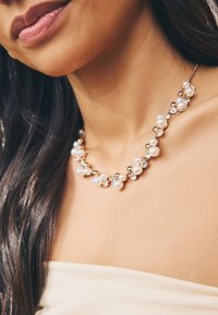 Pearl and crystal necklace featuring white pearls and round crystals, set in gold-tone metal, with a short, rounded design.