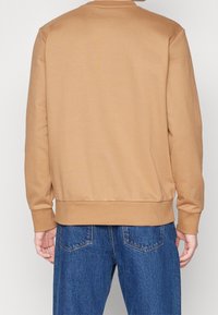 Felpa beige con scollatura rotonda, polsini e orlo a coste, realizzata in tessuto morbido; indossata con jeans in denim blu, che mostrano una vestibilità comoda.