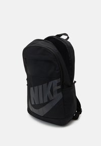 Black backpack made of sturdy fabric, featuring a large gray Nike logo on the front, rounded shape, and adjustable straps.