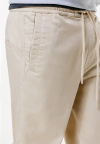 Pantaloni beige realizzati in tessuto morbido, con vita elastica regolabile e tasche laterali, che presentano una raffinata cucitura decorativa.