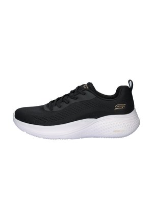 Zapatilla deportiva negra con parte superior de malla texturizada, suela blanca acolchada, diseño con cordones y un acento de logo dorado en el lateral.