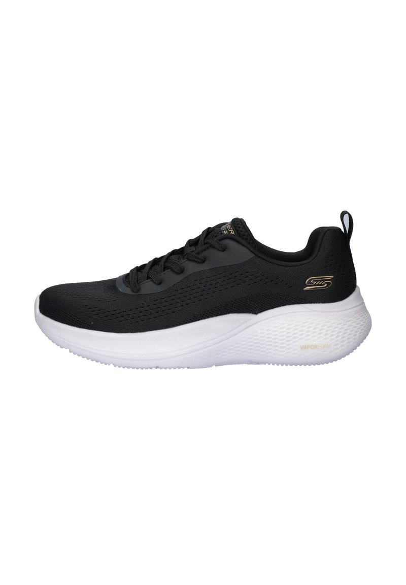 Zapatilla deportiva negra con parte superior de malla texturizada, suela blanca acolchada, diseño con cordones y un acento de logo dorado en el lateral.