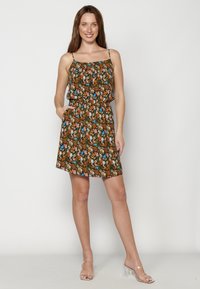 Vestido floral con fondo marrón, tirantes ajustables y cinturilla elástica. Presenta bolsillos y patrones de flores coloridas.