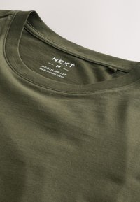 Olijfgroene T-shirt met ronde hals en label "NEXT M Regular Fit Made in Bangladesh" aan de binnenkant van de kraag.