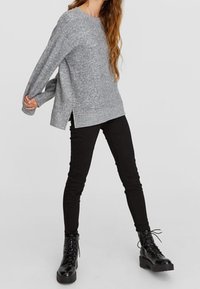 Grå strikket sweater med dropped shoulders og sideslids, parret med sorte skinny jeans og sorte snørebåndsankelstøvler.