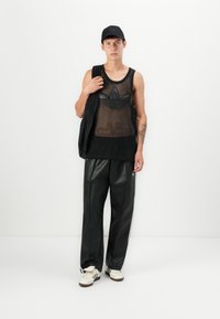 Tricou fără mâneci din plasă neagră cu un logo mare, vestă puffer neagră, pantaloni largi și lucioși negri, și adidași albi cu dungi negre. Căciulă neagră.