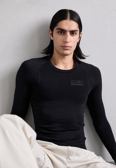 Camisola preta de mangas compridas, feita de um material texturizado e ajustado ao corpo. Apresenta um logo da marca discreto e detalhes em padrão nos ombros.