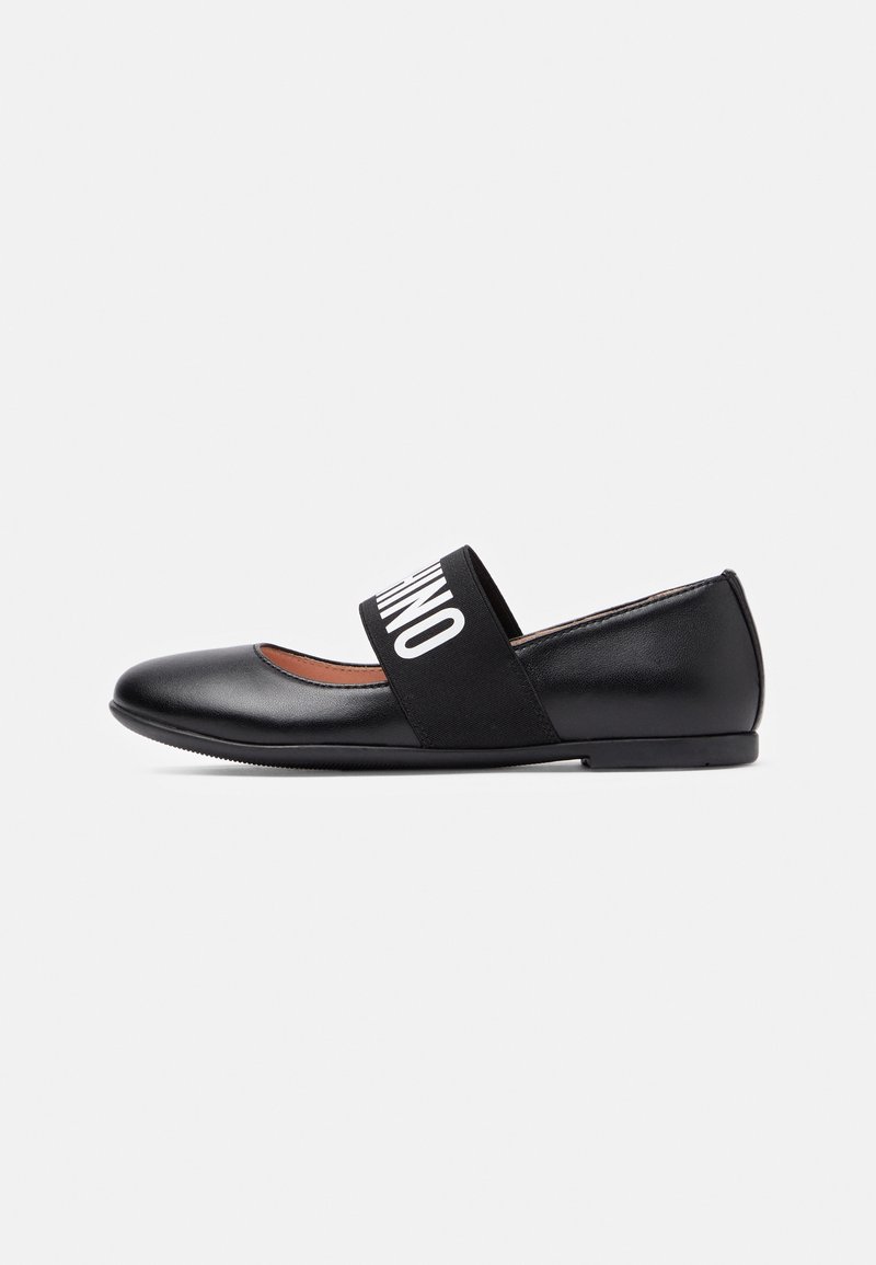 Chaussure plate en cuir noir avec bout arrondi et large bande élastique sur le dessus affichant un texte blanc.