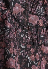 Svart tyg dekorerat med rosa och vita blommönster, med volanger och intrikata sömnadsdetaljer längs sömmarna.