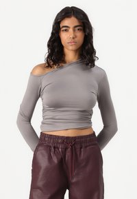 Siva majica s dolgimi rokavi z asimetričnim izrezom, naguban dizajn in mehak tekstil, v kombinaciji z burgundskimi hlačami z elastiko v pasu.