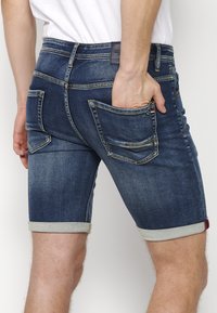 Tmavomodré denim šortky s vyblednutým povrchom, s ohrnutými lemami, viacerými vreckami a kontrastnými švami.