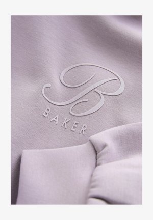 Svijetlopurple tkanina s uzdignutim natpisom „B“ i „BAKER“ ispod. Tekstura je glatka, s suptilnim sjajem.