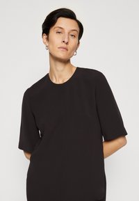 Top negru structurat cu mâneci scurte, guler rotund și linii curate. Realizat dintr-un material neted, având un design minimalist.