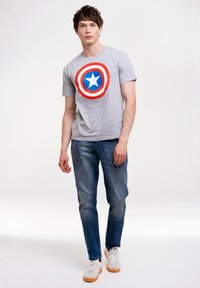 Graues Baumwoll-T-Shirt mit einem roten und blauen kreisförmigen Design und einem weißen Stern in der Mitte, kombiniert mit blauen Jeans und hellen Sneakern.