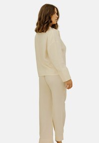 Ensemble de vêtements d'intérieur en maille crème, ample, avec une finition texturée, des manches larges et un pantalon long avec une discrète fente à l'ourlet.