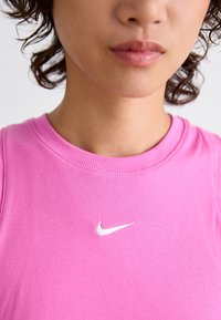 Roza rebrasta majica na bretele s ovalnim izrezom i bijelim Nike logom na prsima. Prikaz izbliza naglašava teksturu i boju.