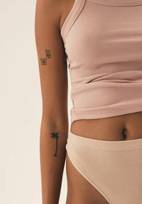 Jasno różowy prążkowany top na ramiączkach i beżowe prążkowane spodnie z wysokim stanem. Widoczne tatuaże motyli i palmy na ramieniu.