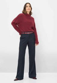 Bordeaux gebreide trui met een hoge hals, gecombineerd met zwarte pinstriped broek en een bijpassende riem, met daaronder puntige bordeauxschoenen.
