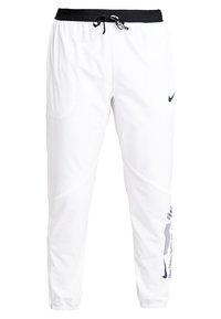 Bílé sportovní kalhoty s černým pasem a šňůrkou, logo Nike na levém stehně a na dolní pravé noze, elastické manžety u kotníků.