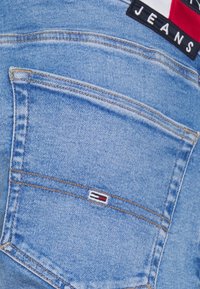 Modré džíny z denimu mají zadní kapsu s prošíváním a malou značkou v červené, bílé a modré barvě. Hladká textura.