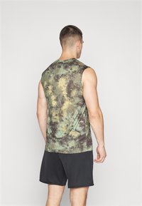 Débardeur de sport sans manches avec un motif camouflage vert, marron et jaune ; tissu léger ; associé à un short noir.