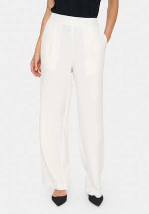 Wide-leg trousers in soft, white fabric with two front pockets and a smooth, tapered waistband. Paired with black shoes.