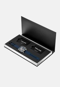 Montre carrée avec un bracelet en silicone bleu, un boîtier en argent et un cadran multicolore. Emballée dans une boîte noire avec deux cartes noires à l'intérieur.