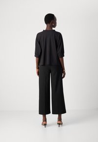 Zwarte top met driekwart mouwen, relaxte pasvorm en ronde hals, gecombineerd met wijde zwarte broek en strappy hoge hakken.