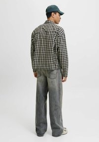 Karierter Hemd in Schwarz und Weiß, lockere Passform, leichtes Material. Kombiniert mit grauen, lässigen Jeans und einer grünen Kappe.