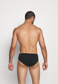 Caleçons de bain noirs en tissu lisse, design taille basse, couverture minimale à l'arrière et ceinture ajustée élastique.