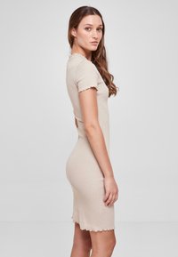 Robe beige côtelée à manches courtes, à bords festonnés et à silhouette ajustée, présentée de profil sur fond uni.