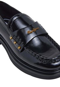 Zwarte gepatineerde leren loafer met een chunky zool, voorzien van een brede band en goudkleurige logo-details, versierd met metalen studs.