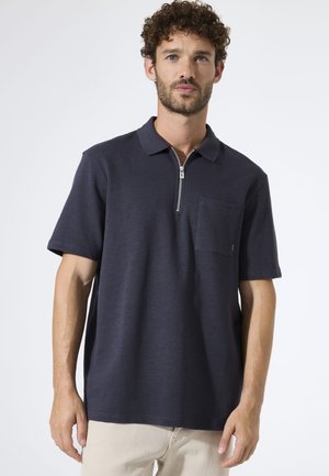 Marineblaues Polohemd mit kurzen Ärmeln, einem Reißverschluss am Kragen und einer aufgesetzten Tasche auf der linken Seite. Strukturierter Stoff mit dezenten horizontalen Streifen.