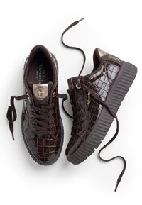 Paire de baskets à plateforme marron foncé avec texture crocodile, semelles épaisses rainurées et lacets lâchement noués sur fond blanc.