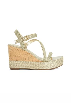 Sandale compensée avec talon en liège et brides métalliques tissées. Bout ouvert et boucle à la cheville. Couleur beige clair avec accents texturés.