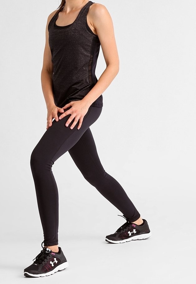 Personne en tenue de sport noire et chaussures de course s'étirant les jambes avec les mains sur la cuisse avant sur fond blanc.