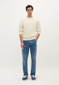 Creme sweatshirt med ribbede manchetter, parret med lyseblå, lige ben jeans. Skoene har blå og hvide detaljer samt snørebånd i sportstil.