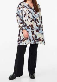 Lange bloemen tuniek met een blauw, bruin en crèmekleurig patroon. Heeft een V-hals en knoopsluiting, gecombineerd met zwarte wijde broek en chunky schoenen.
