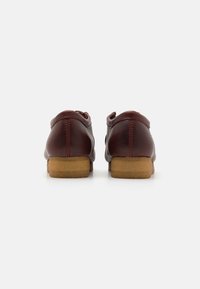 Une paire de chaussures en cuir marron avec des semelles en caoutchouc beige, montrées de dos sur un fond blanc.