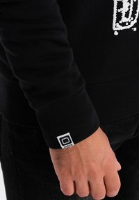 Felpa nera con polsini a coste. Presenta un logo bianco sul davanti e un'etichetta sul polsino. Realizzata in materiale morbido, design aderente.