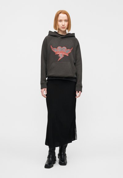 Μαύρο φούτερ με κουκούλα, με σχέδιο καρδιάς από στρας και αστραπή, συνδυασμένο με μακριά μαύρη φούστα και μαύρα μποτάκια αστραγάλου. Λείο ύφασμα, άνετη γραμμή.